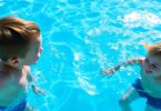 Kids splashing happily in a bright blue swimming pool.