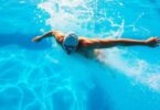 Swimmer powering through clear blue pool water, sun glinting.