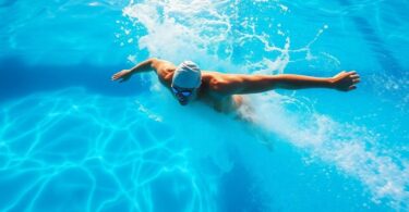 Swimmer powering through clear blue pool water, sun glinting.