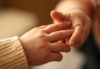 Baby's hand held by adult's finger.