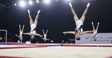 Elite gymnasts performing aerial acrobatics in a training facility.