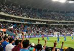 Indian sports fans cheering in a brightly lit stadium.