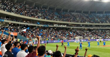Indian sports fans cheering in a brightly lit stadium.