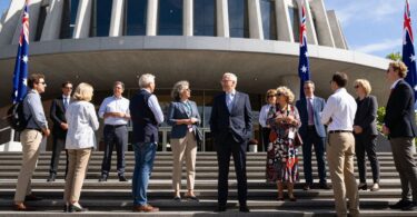 Australians outside a government building with flag and sunlight